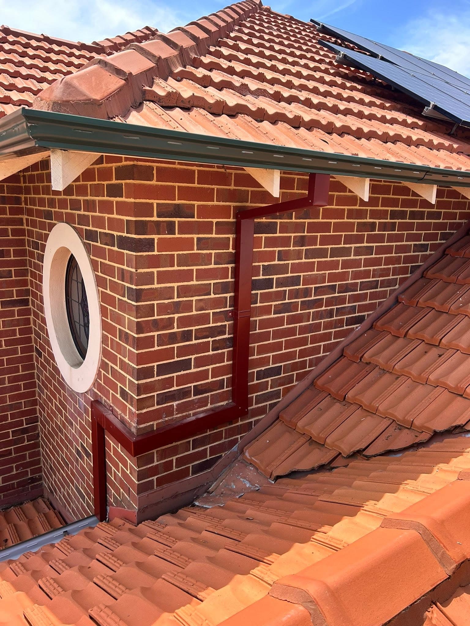 Box gutter and downpipe fitted along a brick wall beside a terracotta tiled roof