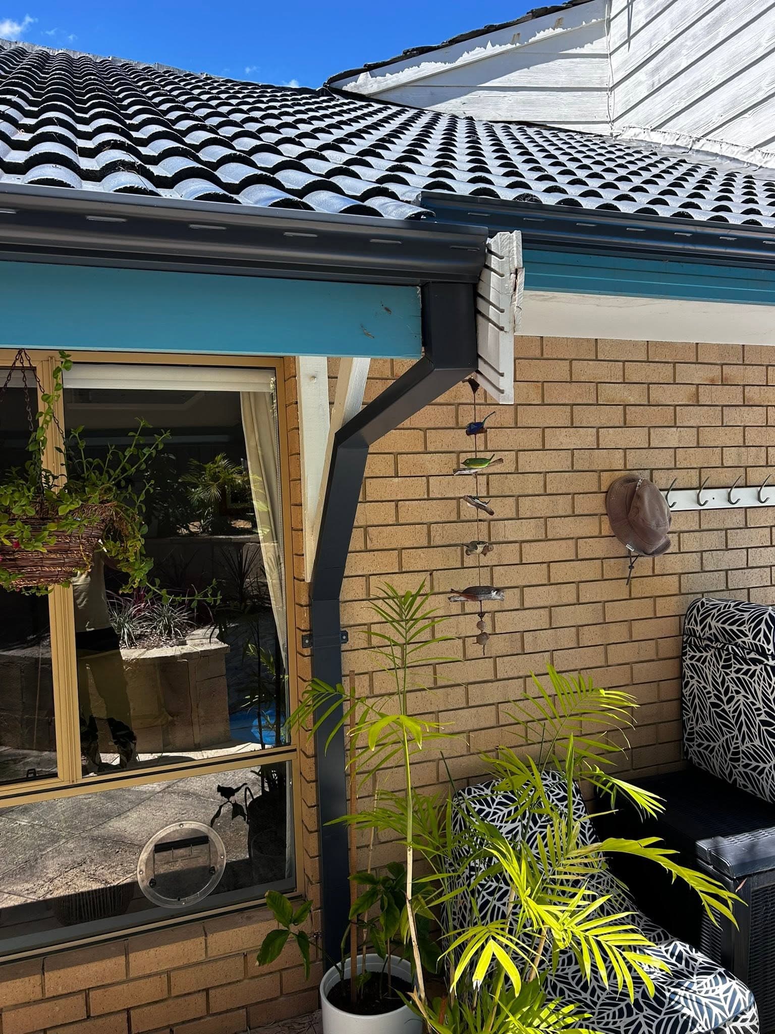 Charcoal tiled roof with new guttering above a brick wall